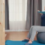 Senior Woman Exercising Using A Resistance Band Whilst Balancing On A Stability Ball