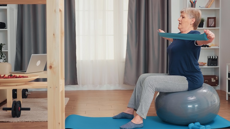 Senior Woman Exercising Using A Resistance Band Whilst Balancing On A Stability Ball